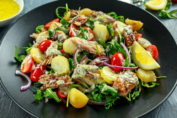 Smoked Mackerel Salad with warm boiled new potato, cherry tomatoes, chopped red onion and Ruccola on black plate.