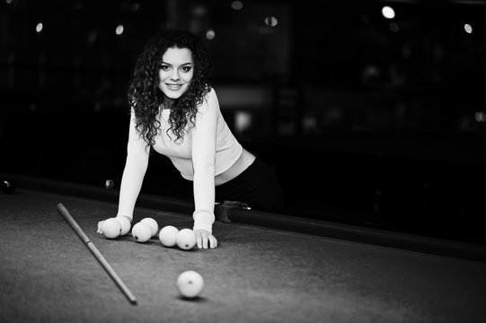 Young curly girl posed near billiard table. Sexy model at black mini mini skirt play russian snooker. Play game and fun concept.