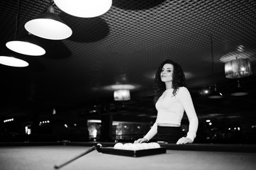 Fototapeta na wymiar Young curly girl posed near billiard table. Sexy model at black mini mini skirt play russian snooker. Play game and fun concept.