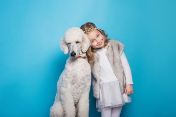 Beautiful little princess with dog. Friendship. Pets. Studio portrait over blue background
