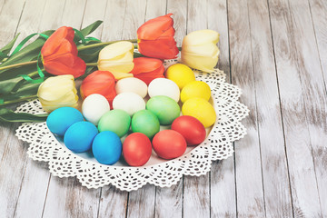 Colored easter eggs with fresh tulips on the white wooden background.