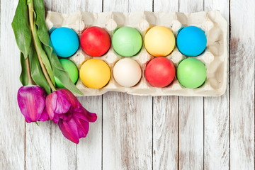 Obraz na płótnie Canvas Colored easter eggs and fresh tulips on white wooden background.
