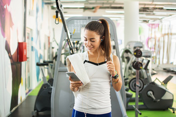 Sportive girl using smartphone and listening to music in a gym.