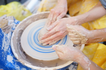 A potters hands guiding a child hands to help him to work with the ceramic wheel