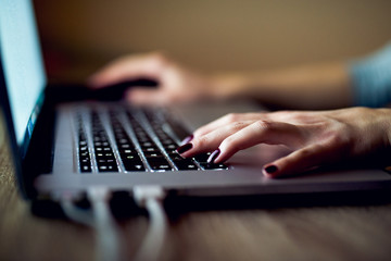 Side shot of female hands typing text on modern laptop keyboard.