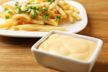 Cheese sauce in small bowl and plate with fries on background