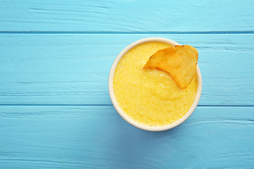 Bowl with tasty cheese sauce and snack on color wooden background