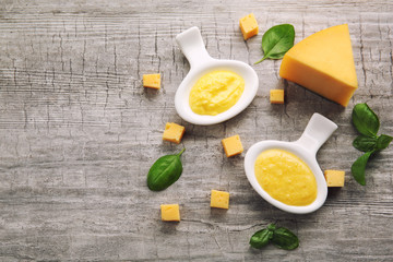 Gravy boats with tasty cheese sauce and basil on wooden background