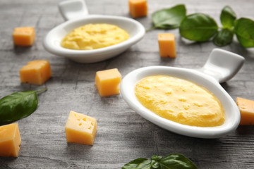 Gravy boats with tasty cheese sauce and basil on wooden background