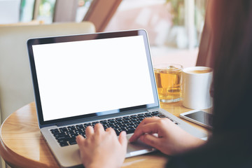 Mockup image of  woman's hands using laptop with blank white screen on vintage wooden table in modern loft  cafe