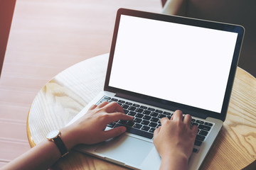 Mockup image of a woman's hands using laptop with blank white screen on wooden table in modern loft cafe