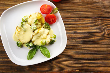 Plate of delicious baked potato with cheese sauce on wooden background