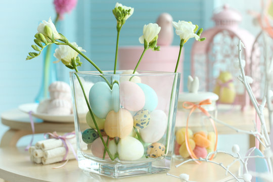Painted eggs in glass vase and Easter symbols on wooden table