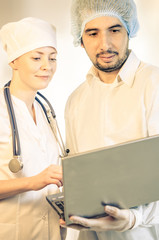 Group portrait of medical doctors in hospital looking at the laptop. Man wearing surgeon coat and woman wearing white cap. Focus on man doctor. Toned.