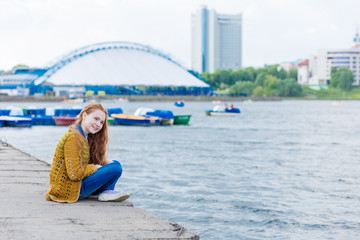 Red-haired girl with freckles sitting on the seashore