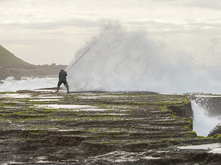 Spray and breaking wave challenge a lone fisherman at spring-low tide at Reunion Rocks south of...