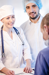 Group portrait of medical doctors in hospital having consultation with patient. Man wearing surgeon coat and woman wearing white cap. Focus on woman doctor.