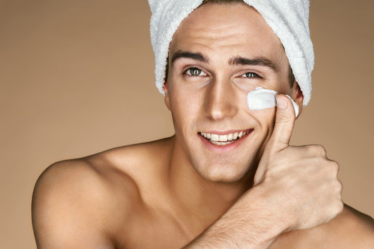 Handsome young man applying cream to his face. Portrait of a smart man with perfect skin. Skin care concept