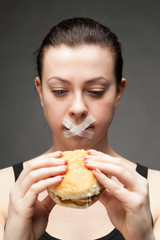 Diet concept: woman holding a burger with mouth sealed