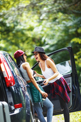 Naklejka premium Two young women with suitcases on car trip.They are standing by the car and resting after long ride and making fun.Coffee break.