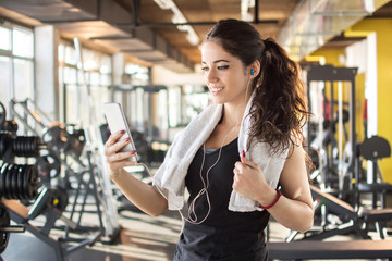 Attractive girl with earphones holding mobile phone to play favorite songs at gym.