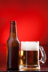 A full mug of beer with bottle isolated on red background