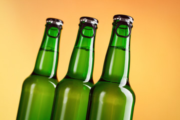 Three green beer bottles isolated over orange background