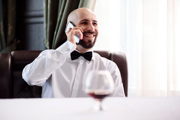 A bald man in a restaurant talking on the phone.