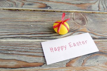 Пасхальное цветное яйцо является символом праздника.  Яйцо перевязано красной лентой. Яйцо и письмо с пожеланием  находятся на деревянном столе