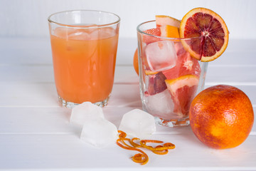 Full glass of grapefruit juice and glass of sliced fruit. Grapefruit sicilian orange with ice. White wooden background