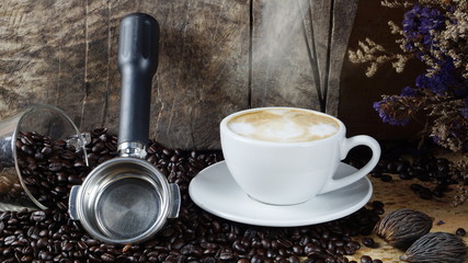 Hot cappuccino with streamed milk. Pour the hot latte art by milk. A cup of strong espresso coffee put on the wood table with shiny dark roasted Italian coffee beans. Aroma and flavor coffee beverage.