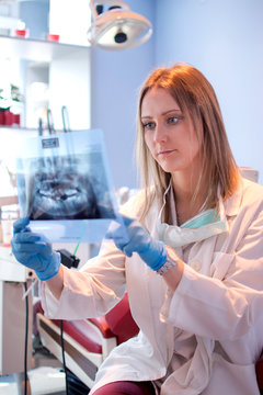 Female dentist examining x-ray image of teeth in dental clinic.