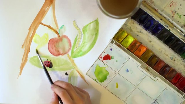 A young girl draws watercolor paint on a white sheet of paper. Using a brush. Butterfly. Top view.