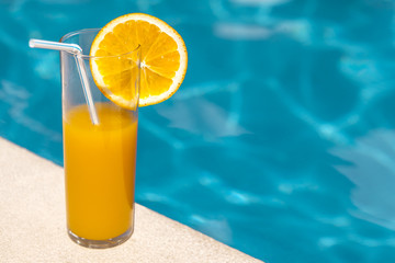 Glass of orange juice with orange slice near the swimming pool