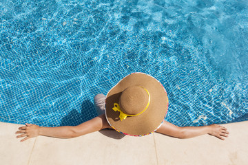 Top view of a woman in hat relaxing on swimming pool