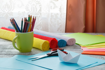 Set of origami boats and square sheets of colored paper on a wooden table. How to make a simple...