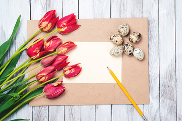 Easter eggs,beautiful red tulips, blank note on wooden background.