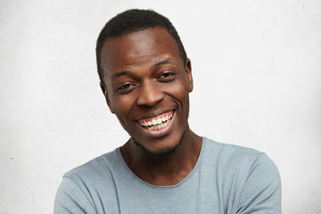 Are you kidding me? Seriously? Headshot of handsome emotional young Afro-American man with cheerful happy smile, laughing at joke, having amazed and stunned look, posing at white wall. Body language