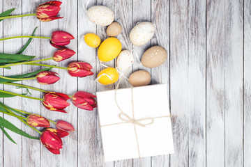 Easter background. Colored easter eggs and red tulips on wooden background. Top view.
