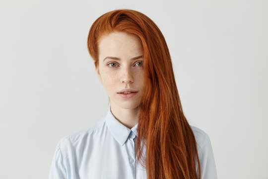 Gorgeous redhead student girl with long loose hairstyle wearing light-blue formal shirt getting ready for exams at college. Beautiful ginger young female of European appearance posing indoors