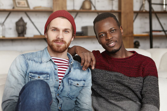 Happy homosexual interracial couple having rest indoors. African American  male resting elbow on shoulder of his handsome stylish partner in trendy  clothes, both looking at camera with joyful smiles Stock Photo |
