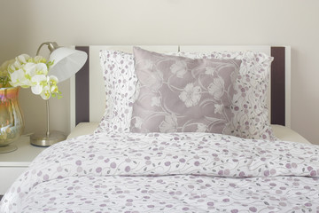 Tiny lavender pattern style bedding in bedroom with white orchid next to bed.