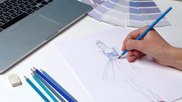 Designer with a pencil sketch decorates dresses in blue. Close up