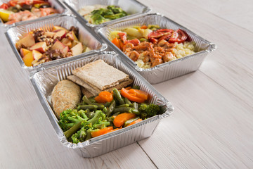 Healthy food take away in foil boxes on wood background