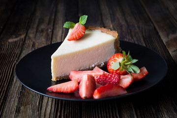 Cheesecake with fresh strawberries on black plate. Wooden table background