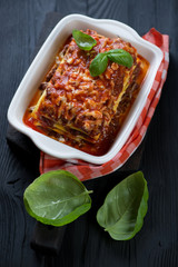 Baking dish with lasagna bolognese and fresh green basil on a black wooden background, studio shot