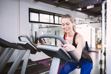 Fototapeta premium Smiling woman riding an exercise bike in gym