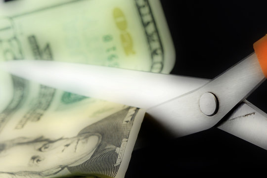 Scissors cutting American currency twenty dollar bill - Budget cuts financial crisis concept