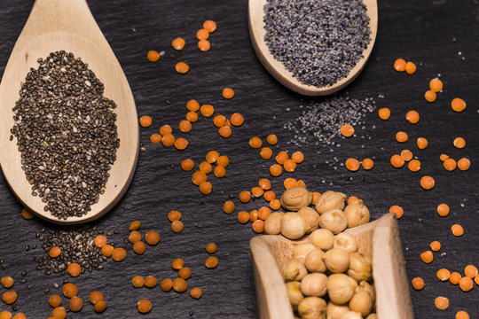 Chia and poppy seeds, red lentils and chickpeas with wooden spoons on black background