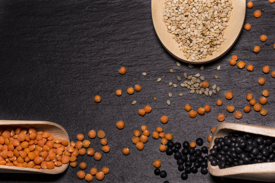 Sesame, red and black lentils with wooden spoons on black background